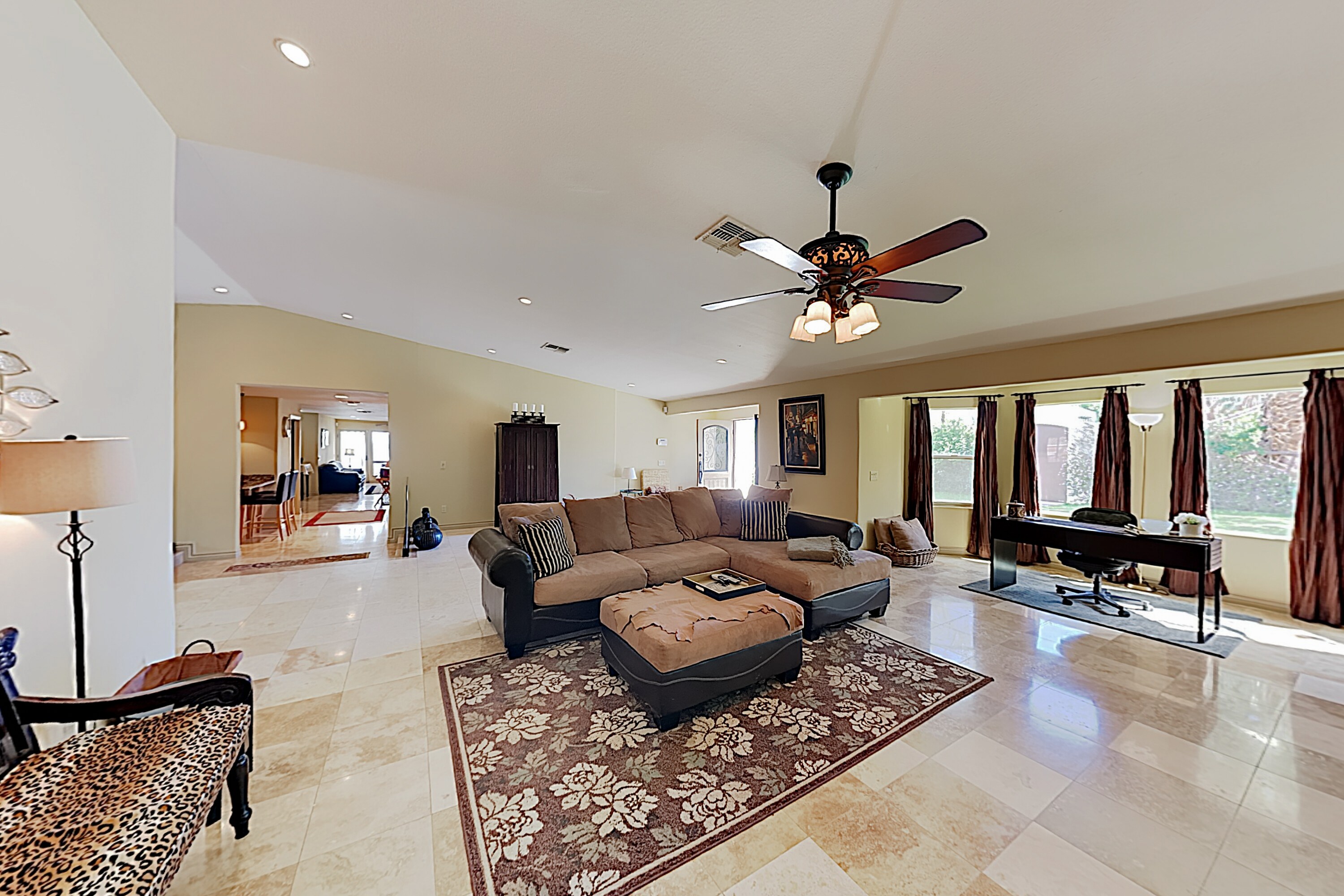 Travertine flooring lines the airy Great Room, furnished with a sectional and a desk.