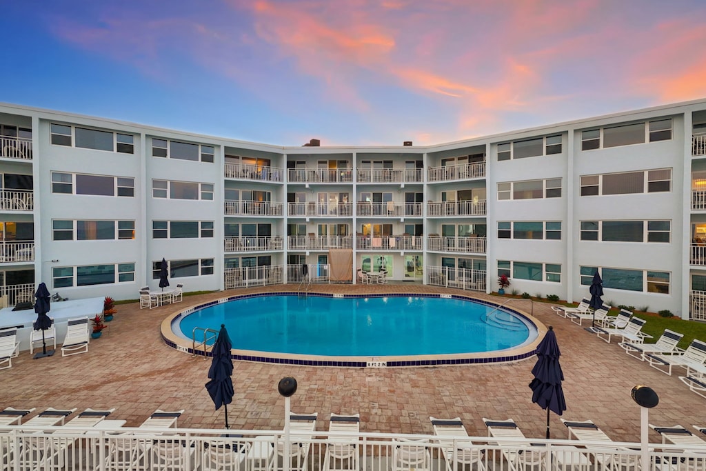 Evening view of the inner courtyard showing a circular swimming area centered between residential wings, with perimeter seating and soft ambient lighting under a pastel sky.