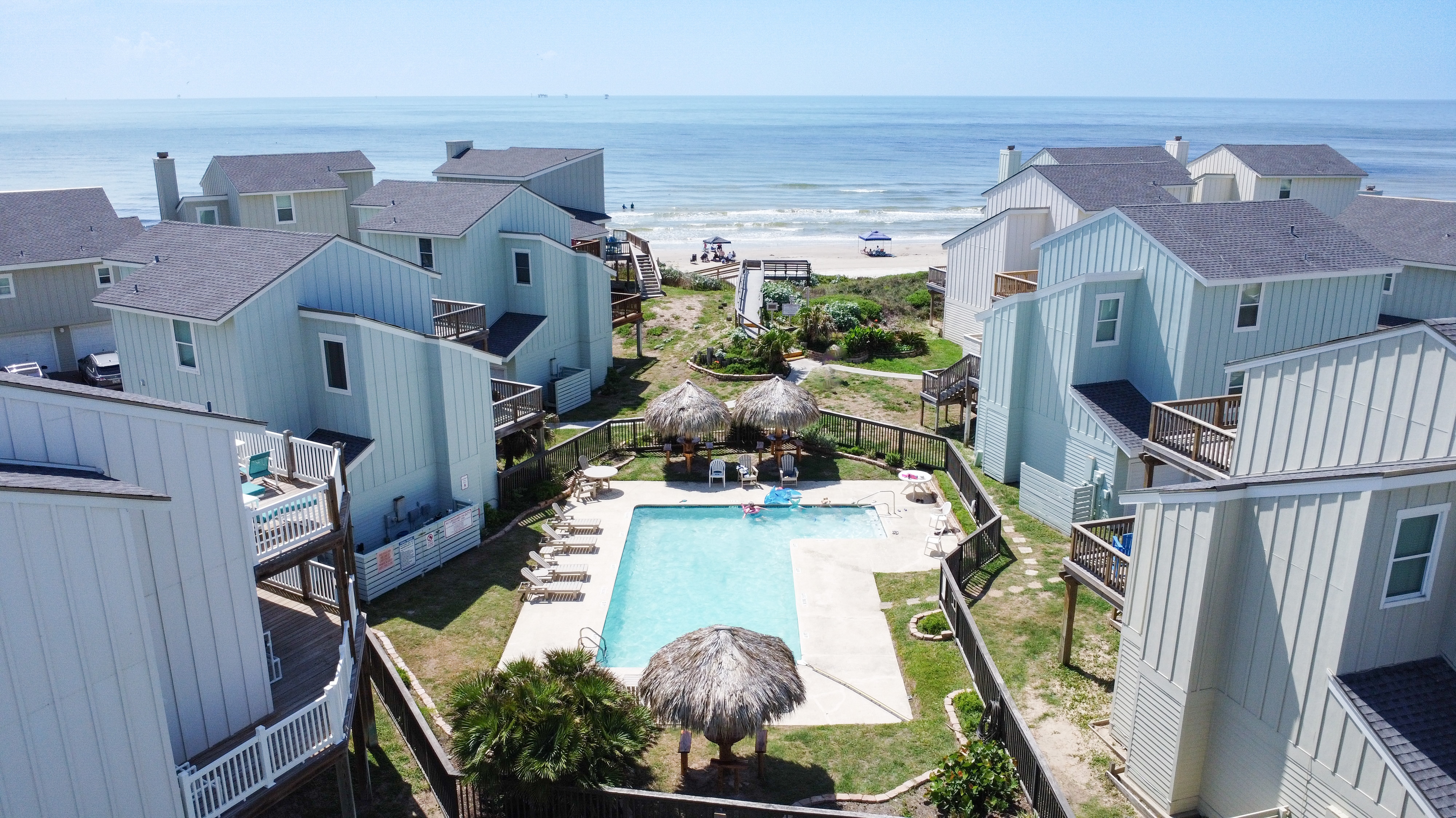 Inviting community pool with clear blue water, surrounded by comfy loungers and straw covered structures.