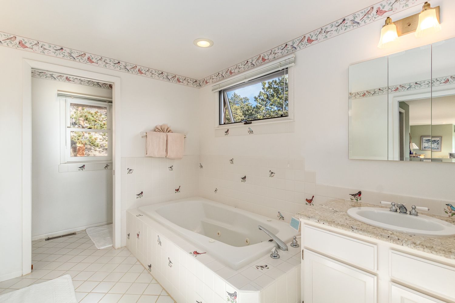 Bishop's Retreat - Master Bathroom - 2 sinks, jetted tub, window above tub. Quirky and fun bird decor adorns the walls and tub tiles.