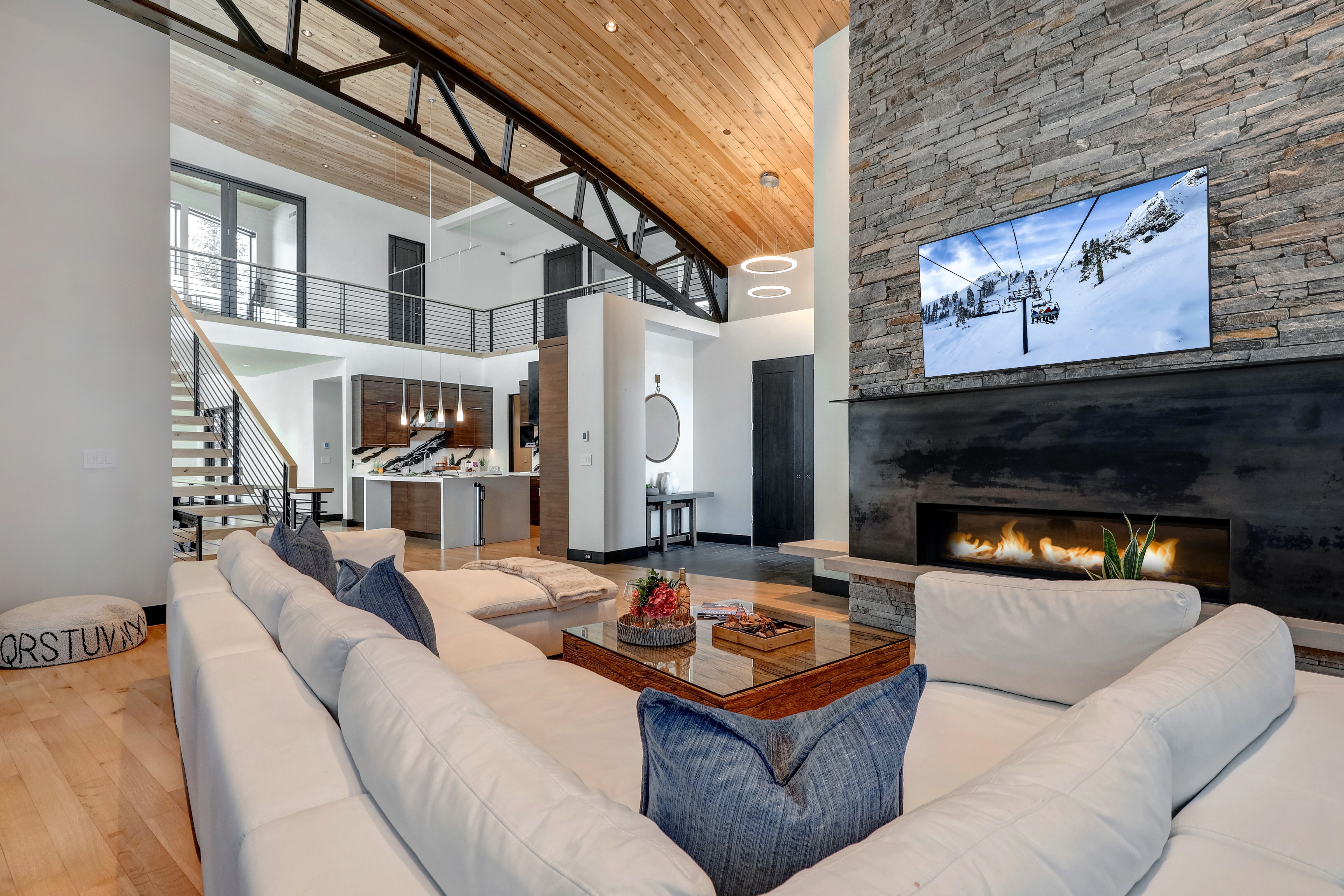 Main Level Living Room with vaulted ceilings, plush over-sized sectional, 65" Samsung TV, elegant gas fireplace, and indoor/outdoor glass patio doors
