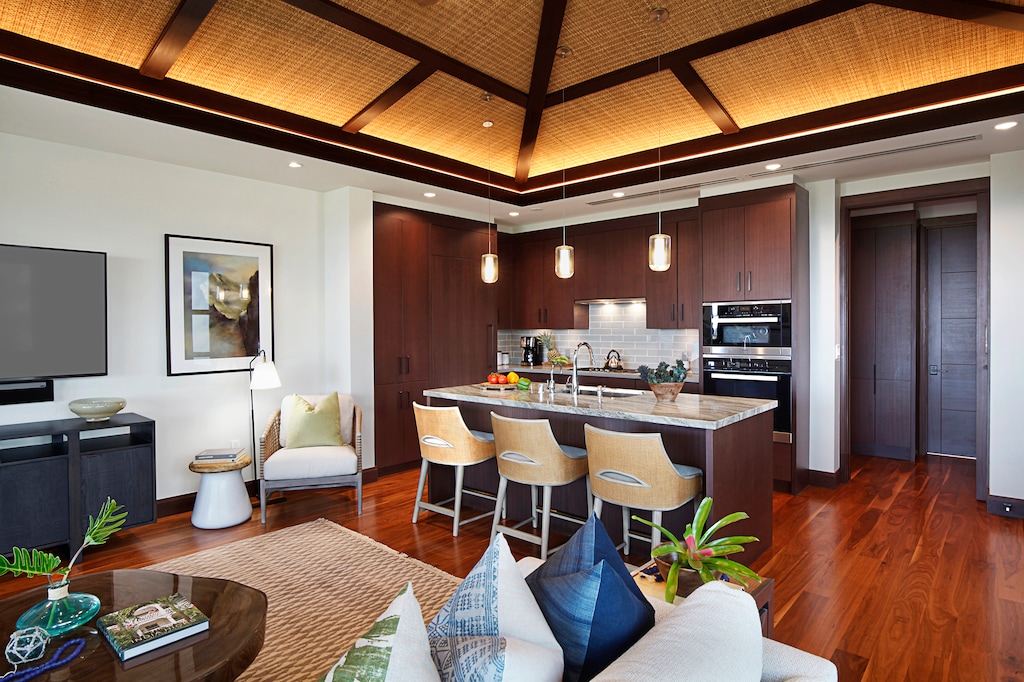 The home's polished ocean-view kitchen with gleaming granite counters, custom cabinetry, and large island with bar seating flows effortlessly into a sophisticated living space, which in turn flows out to a spacious covered lanai, blurring the lines between