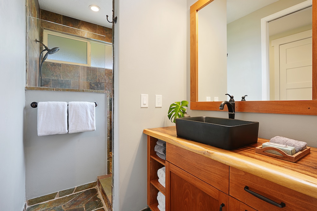 Your private bathroom features modern touches with a sleek black vessel sink, warm wood vanity, and rejuvenating walk-in shower.