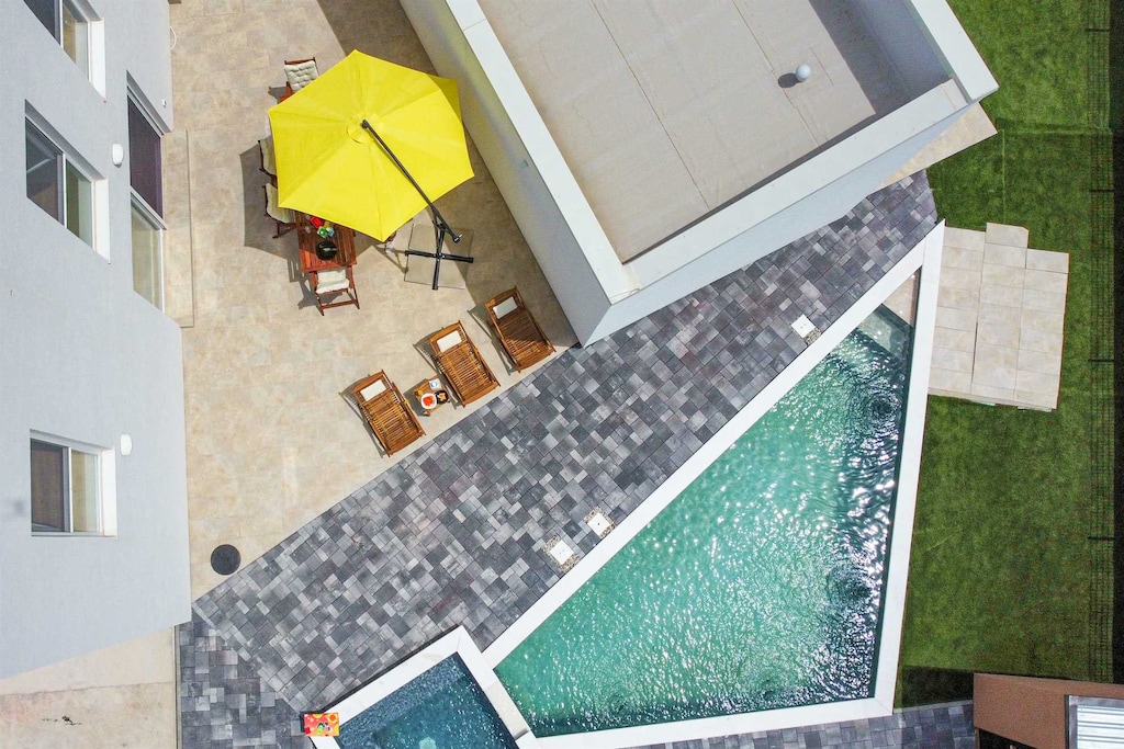 Uniquely shaped pool with conjoined whirpool, outdoor seating and dining area with parasols and sunloungers