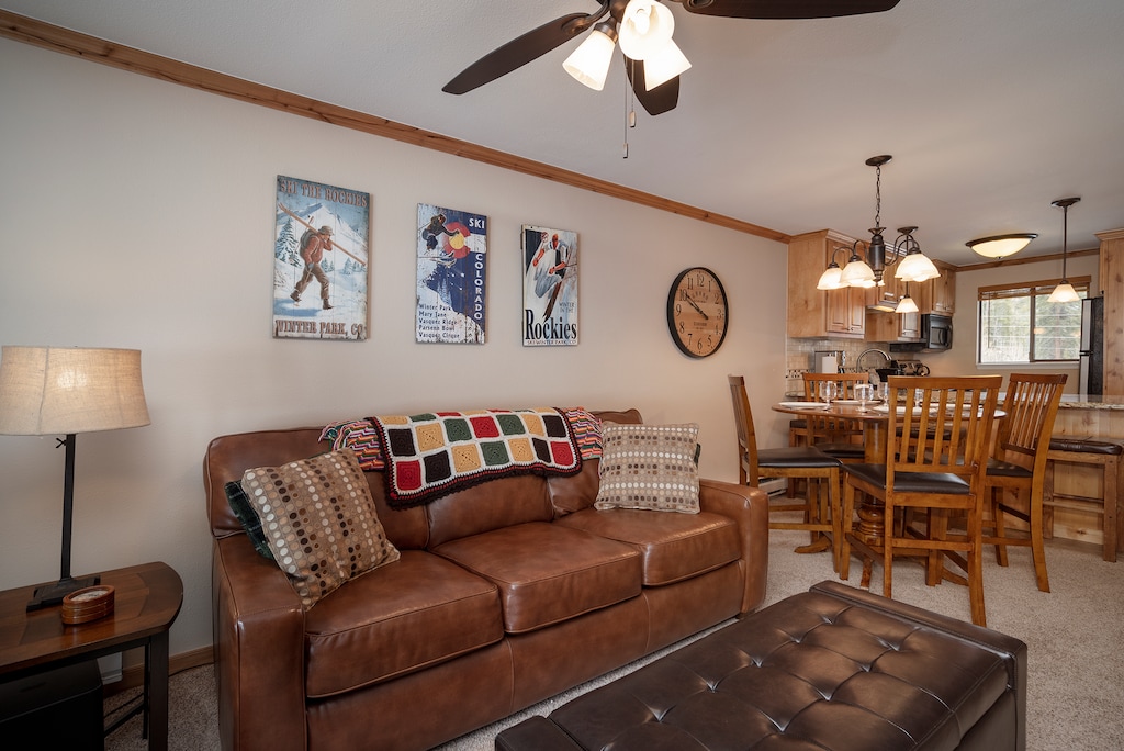 Relax in your cozy mountain retreat featuring a leather sofa, ski-themed artwork, and open kitchen perfect for après-ski meals together.