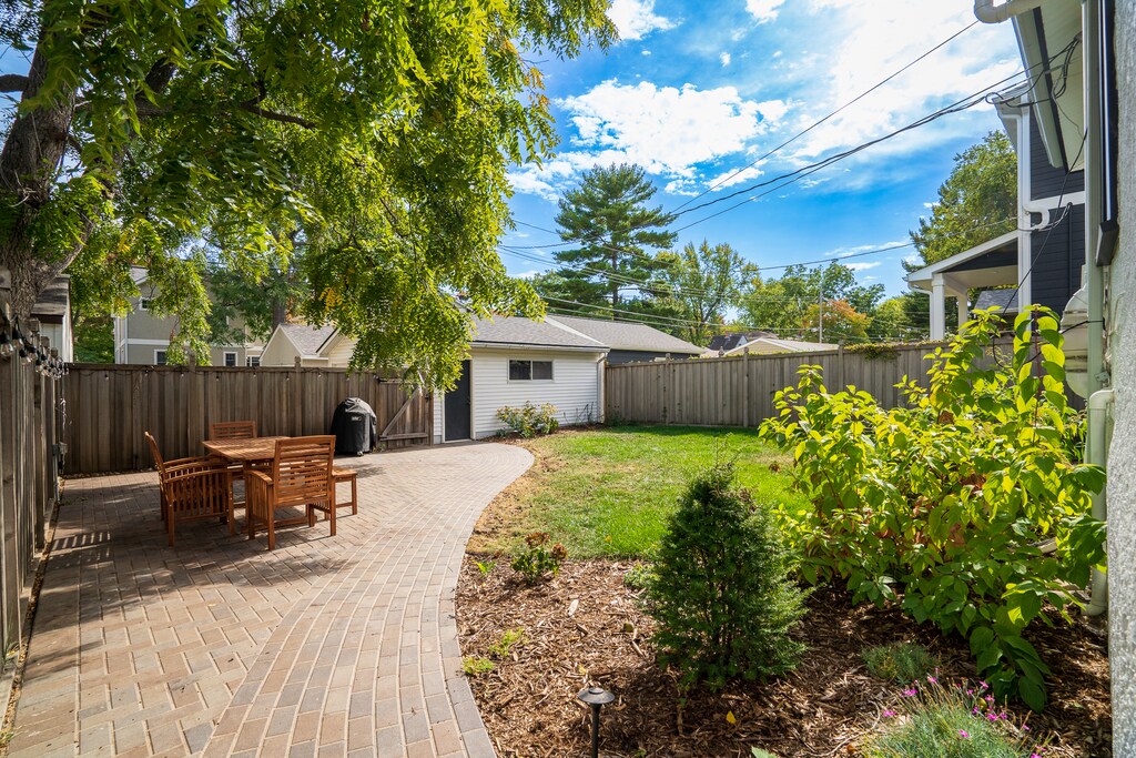 Relax in your private backyard oasis with paved patio, outdoor dining space, and lush garden beds surrounded by peaceful greenery.