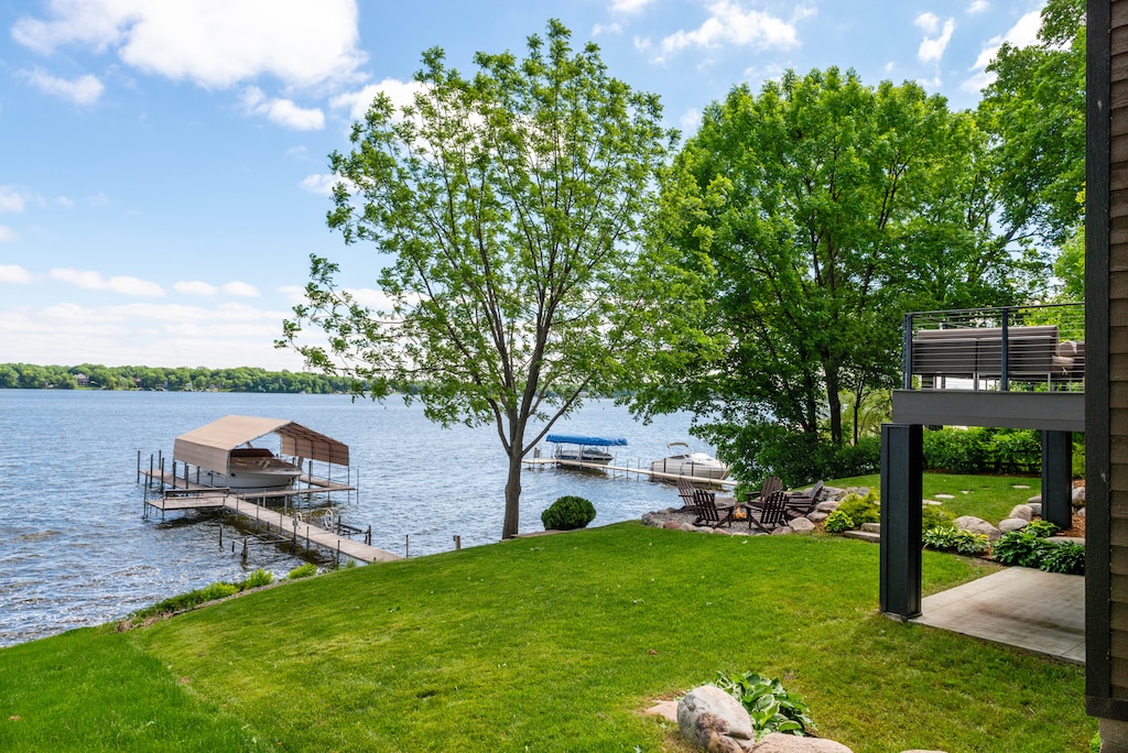Stunning lakefront property featuring private dock, boathouse, and pristine lawn leading to crystal-clear waters surrounded by lush forest.