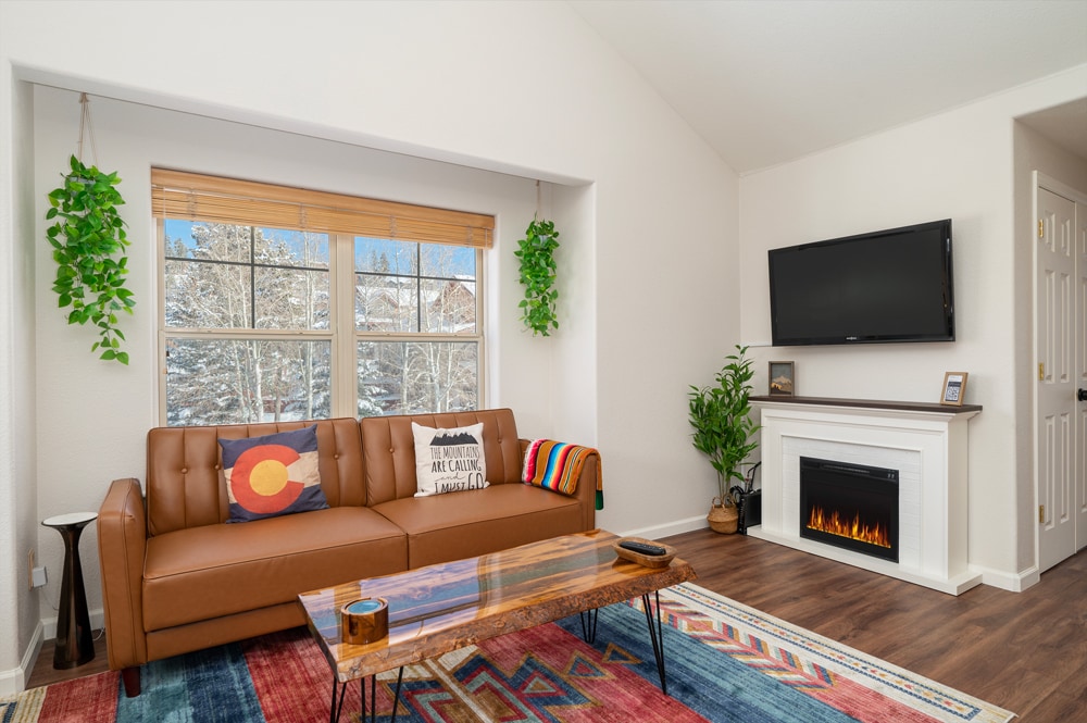 Cozy up in your stylish living space with a crackling fireplace, vibrant furnishings, and peaceful winter views through the window.
