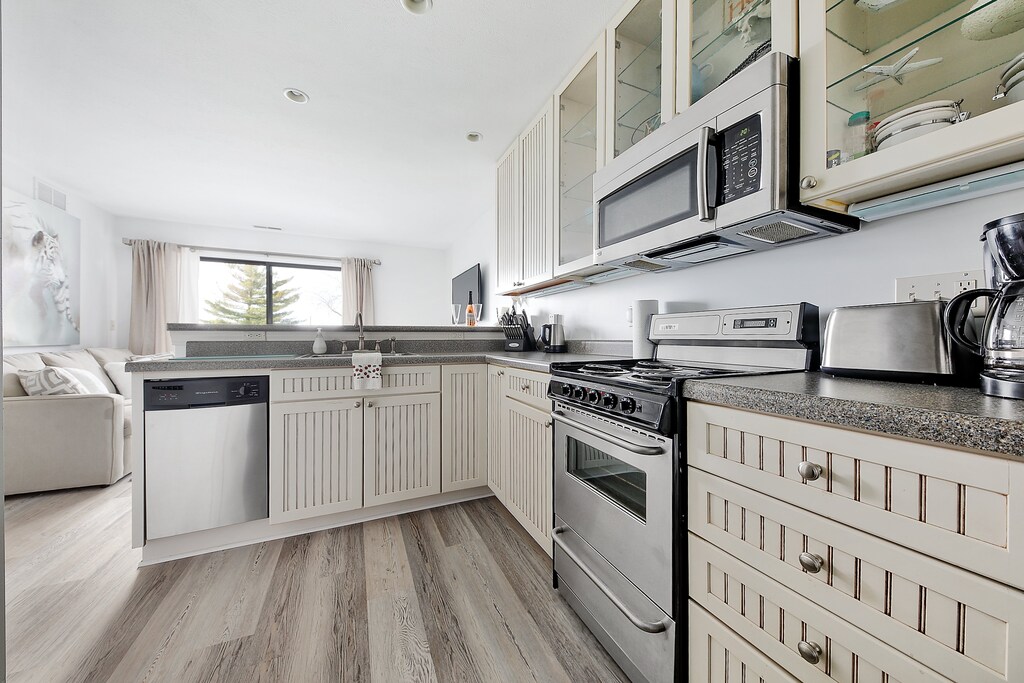 Observing from the kitchen in the unit, you'll find a stove with four burners, a microwave, and a fully equipped kitchen. The living space extends to a balcony, featuring a sofa and a flat-screen TV.