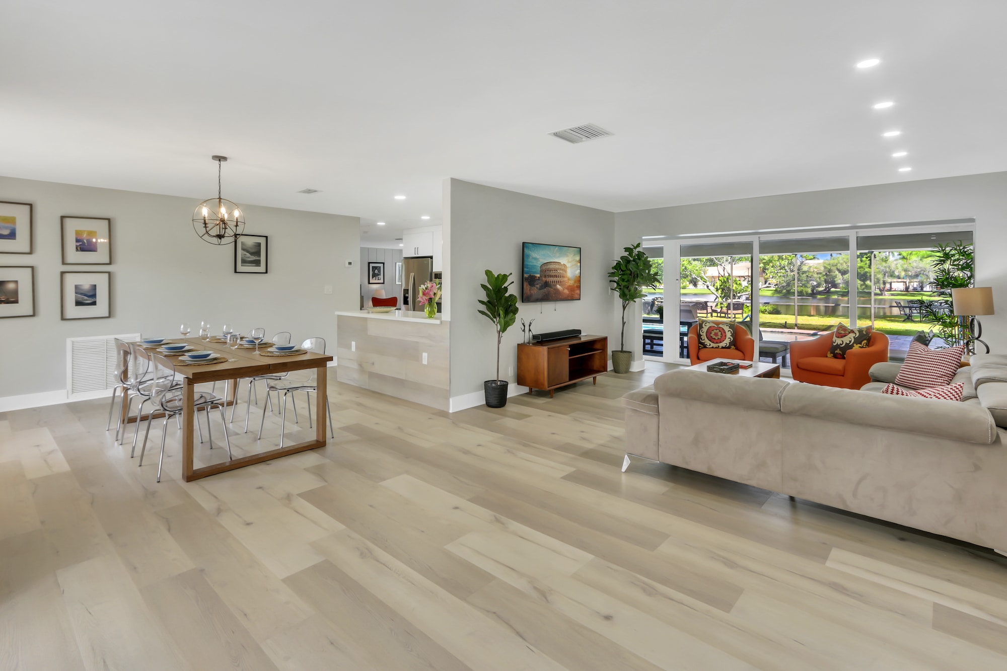 Open floor plan shows living room with tv, dining table for six, and a direct view of the pool and lake.