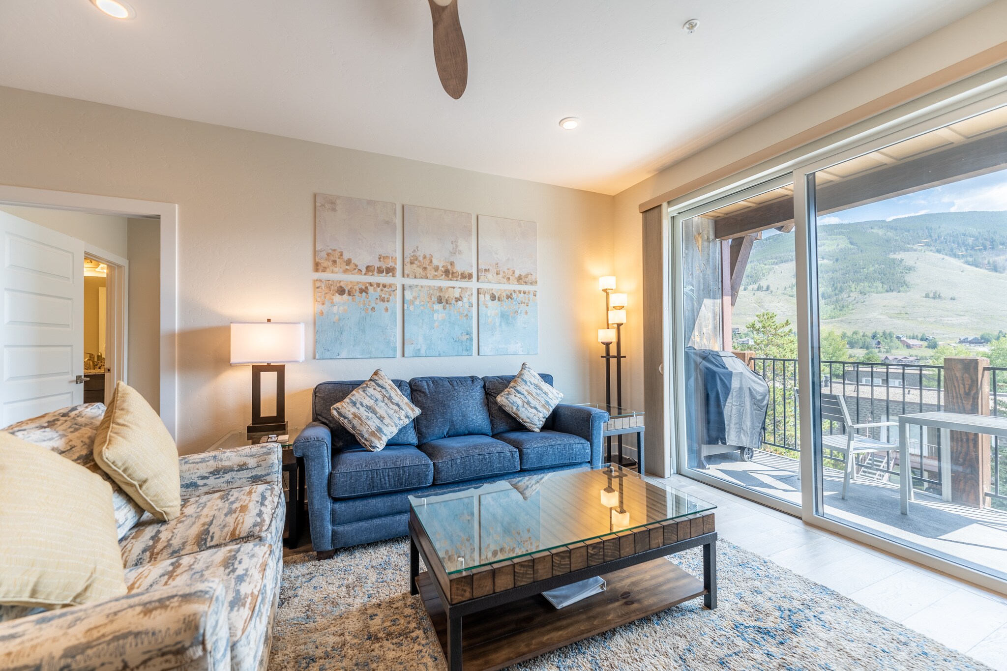 Living area featuring cozy furnishings, a gas fireplace, ceiling fan, and balcony access. 