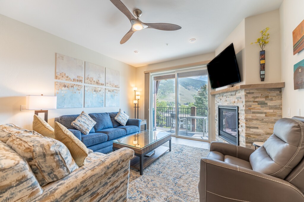 Living area featuring cozy furnishings, a gas fireplace, ceiling fan, and balcony access. 