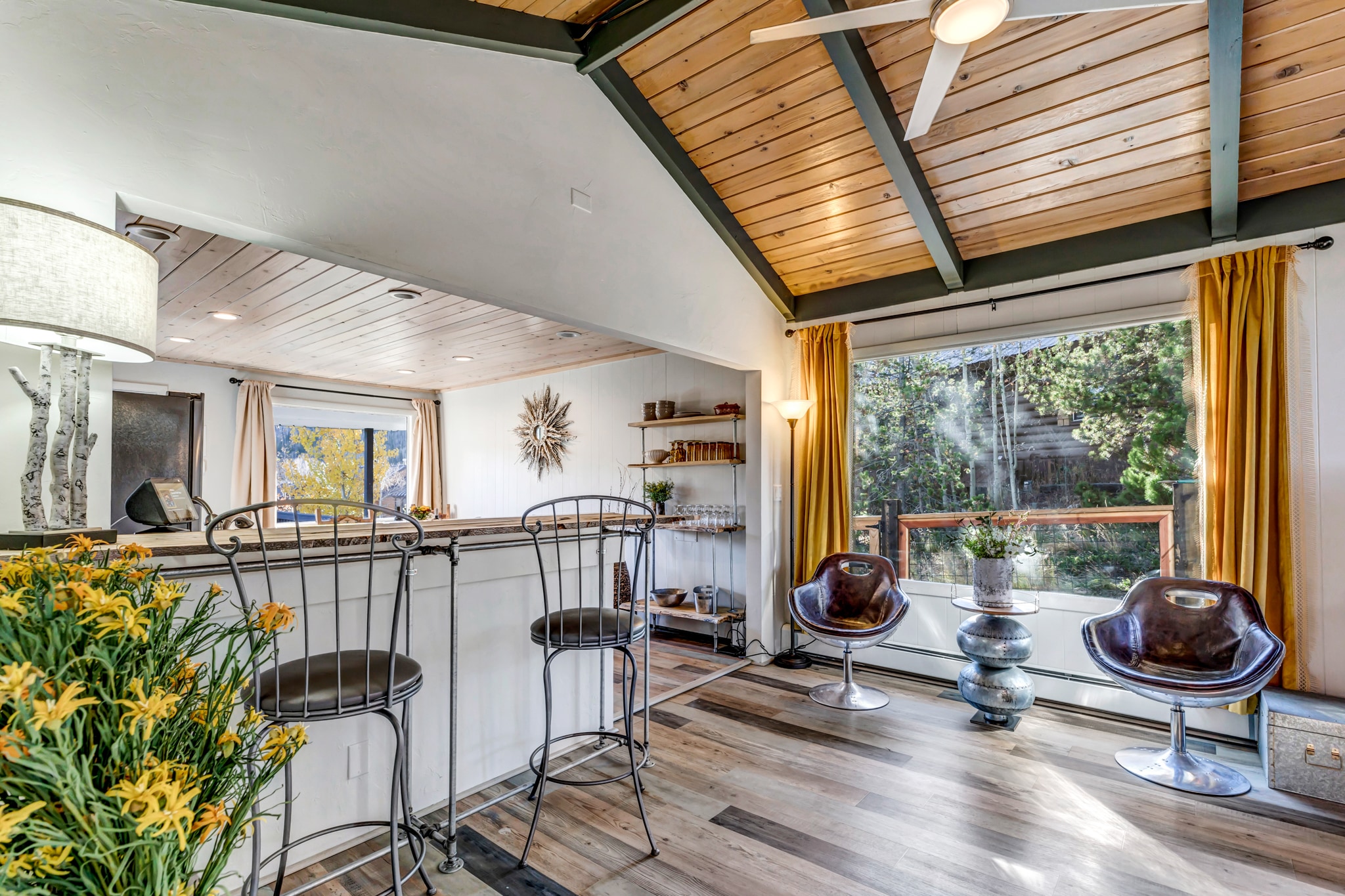 Main floor living area with cedar ceilings, beams, large window with seating area and passthrough bar into the kitchen