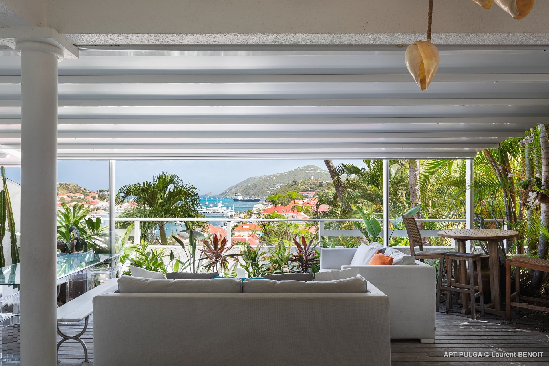 Lounge area with sofa on the covered terrace, facing the panoramic view over Gustavia. 