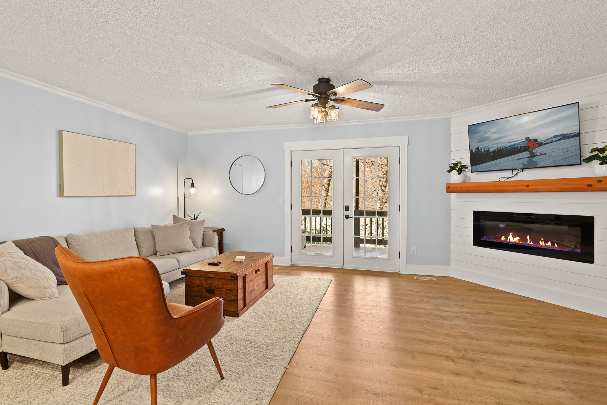 Unwind in style: a roomy living space featuring a wide flat-screen TV, a cozy fireplace below, and elegant glass panel double doors, inviting comfort with a touch of sophistication.