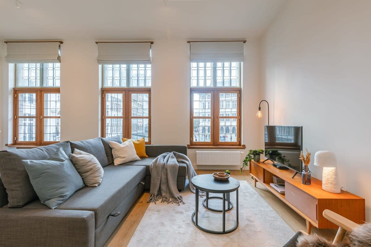 The living room is warmly furnished and spacious, and it has an outside view of the Grand Market of Antwerp.