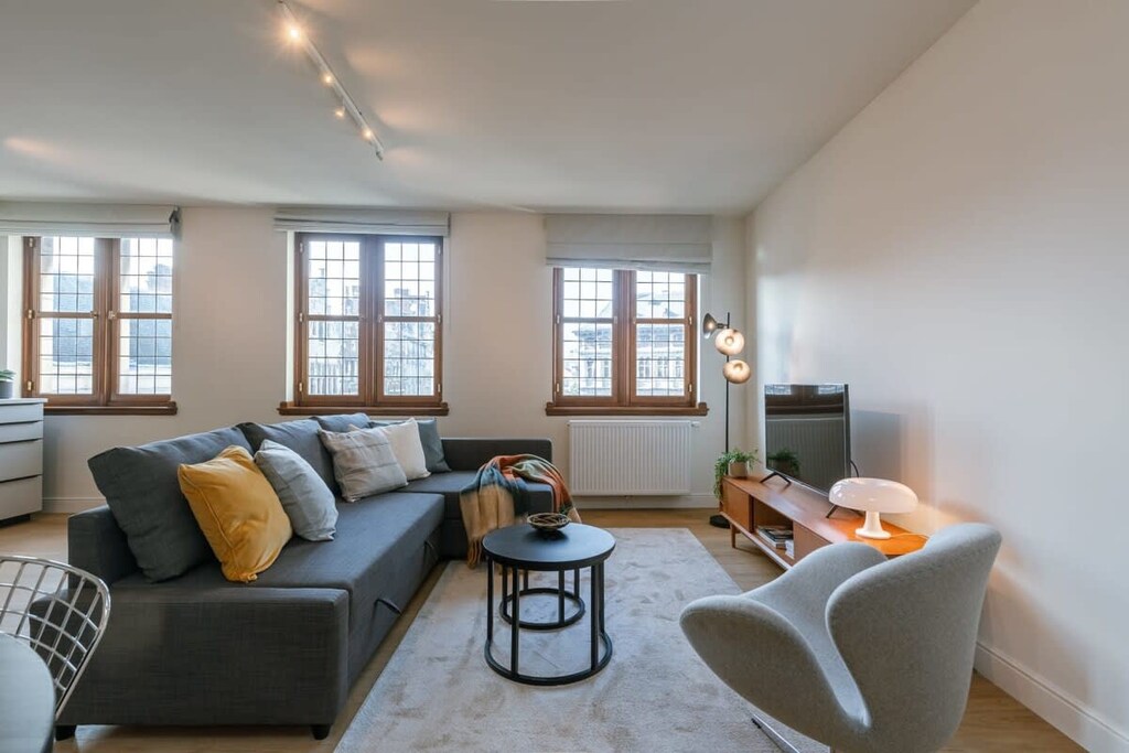 The living room is warmly furnished and spacious, and it has an outside view of the Grand Market of Antwerp.