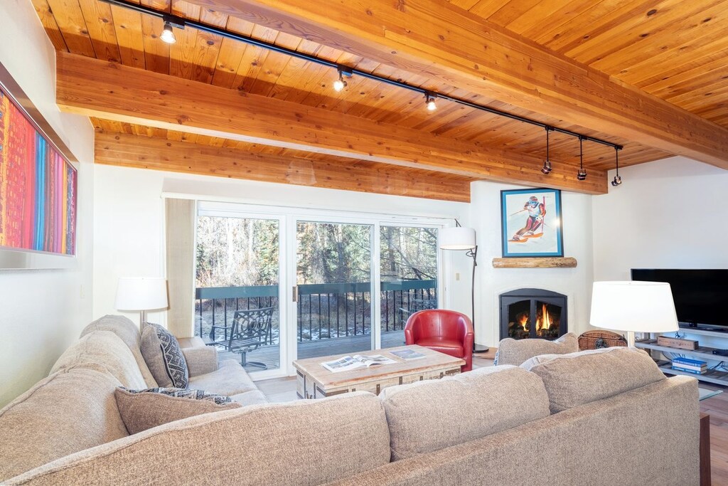 The living area has a large L shaped sofa with glass doors opening out to a deck.