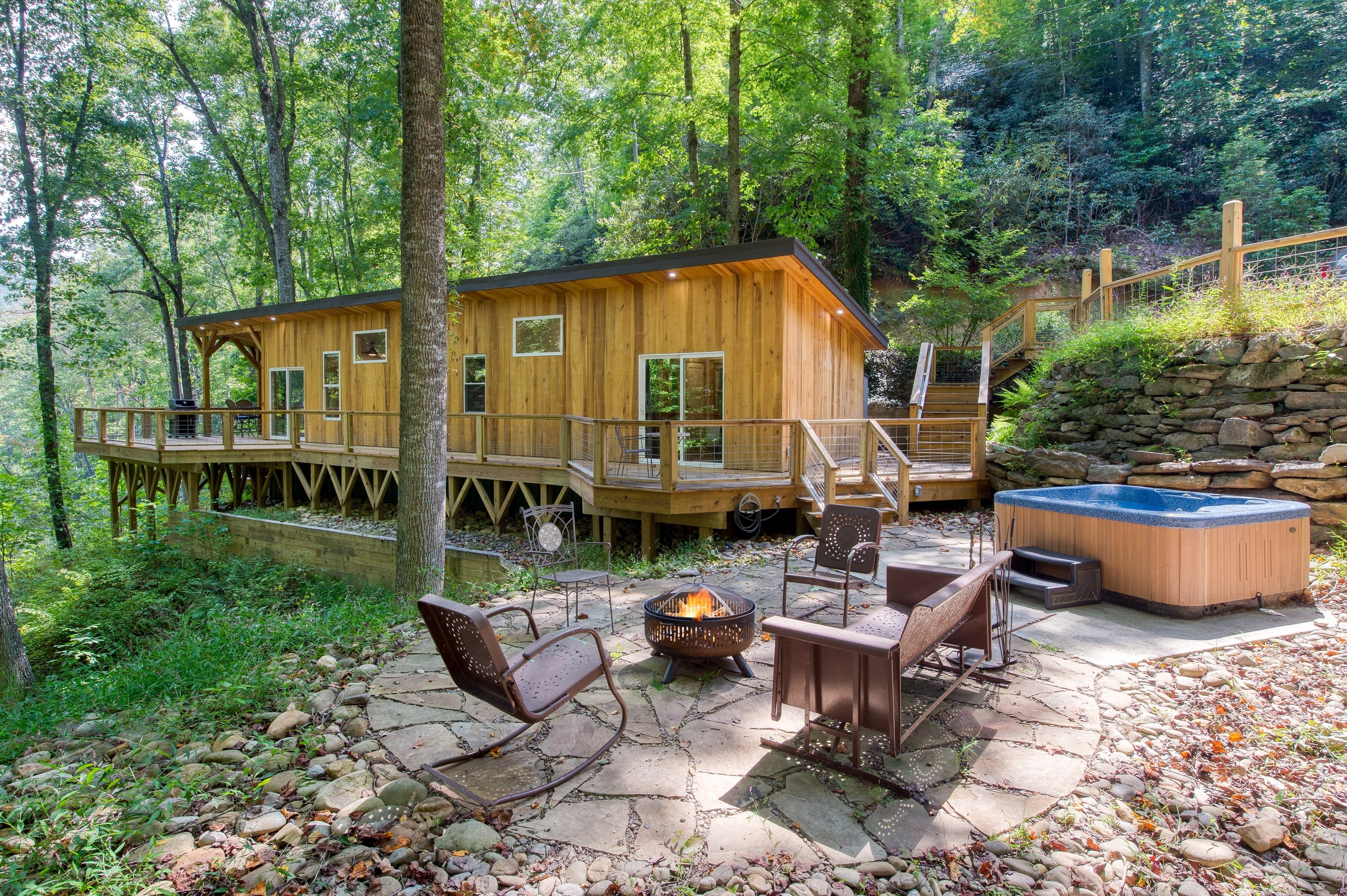 Stunning outdoor space is surrounded by trees and offers lounge areas and a hot tub.