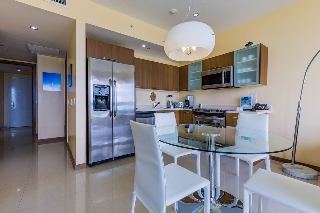 Your fully-equipped modern kitchen and dining space await—sleek stainless appliances, warm wood cabinetry, and a stylish glass table invite easy mornings and relaxed meals.