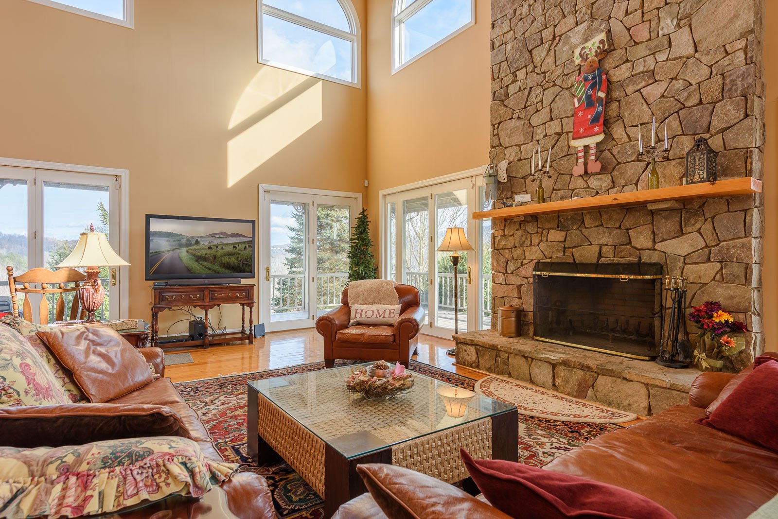 Main Level Living Room includes a Floor to Ceiling Stone Fireplace, Large HDTV, and Deck Access