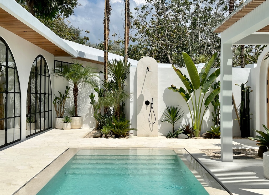 An outdoor area with a tropical garden, terrazzo swimming pool, and a limestone outdoor shower