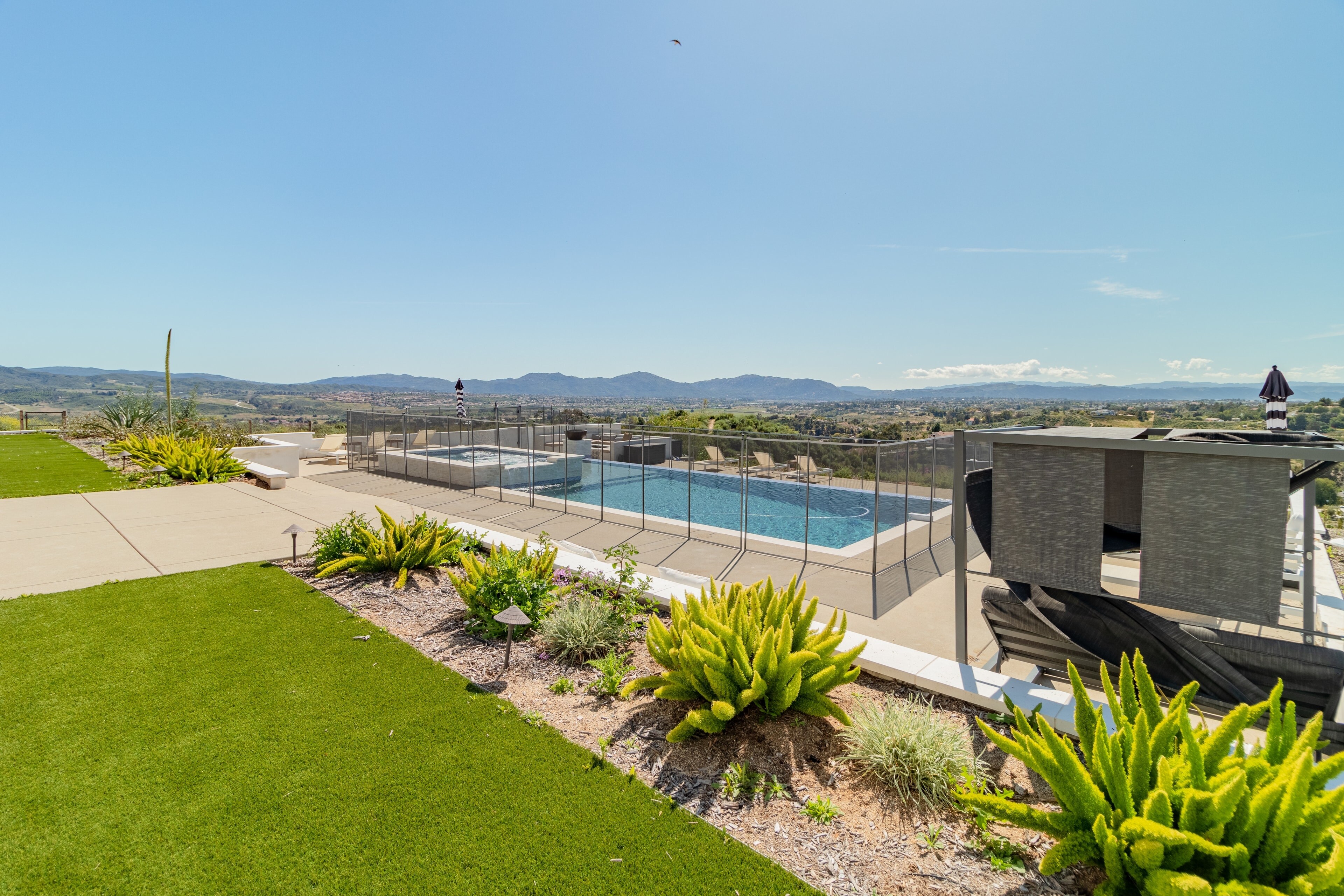 The backyard features fenced in pools, a hot tub, green space with lawn games, an electric firepit, and an outdoor dining table.