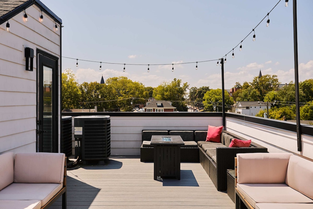 Expansive rooftop retreat with cozy sectional seating, a fire table for evening relaxation, and string lights adding a charming glow—perfect for enjoying views of the surrounding neighborhood.