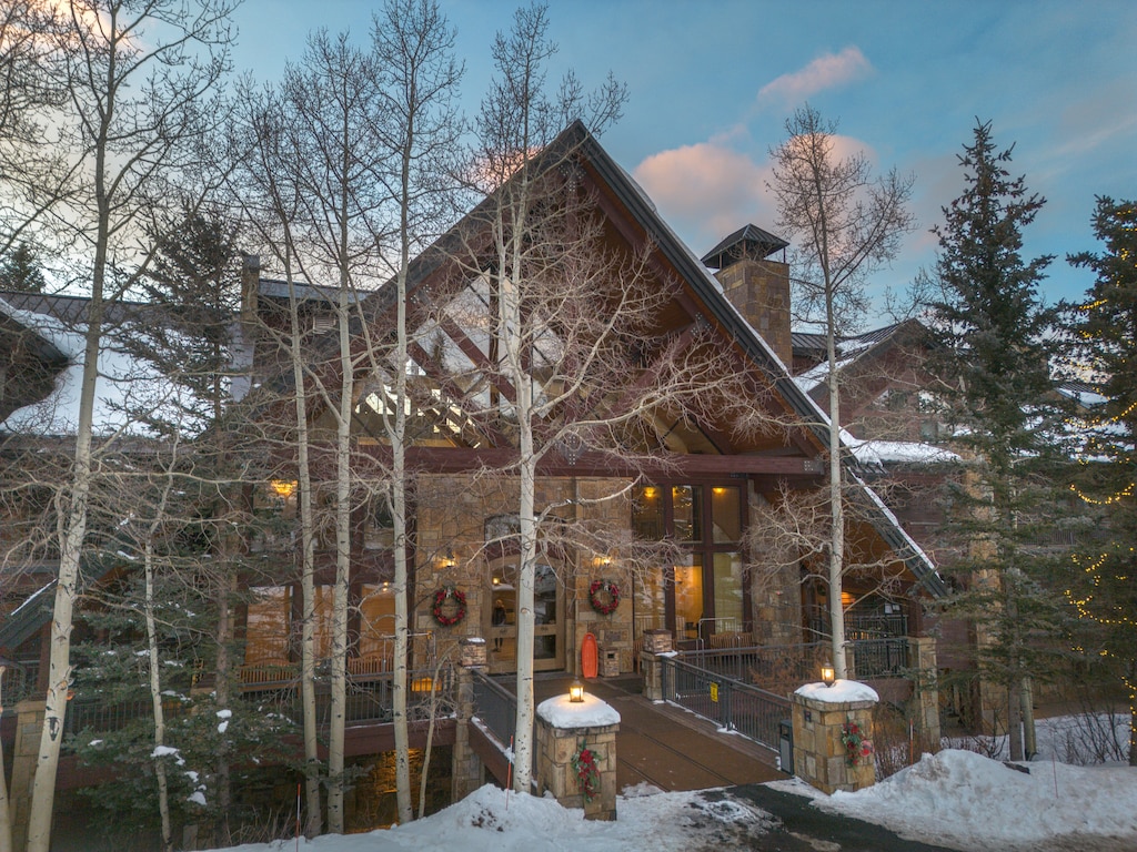 Stunning mountain lodge nestled among snow-dusted aspens, featuring rustic stone architecture and warm holiday touches.