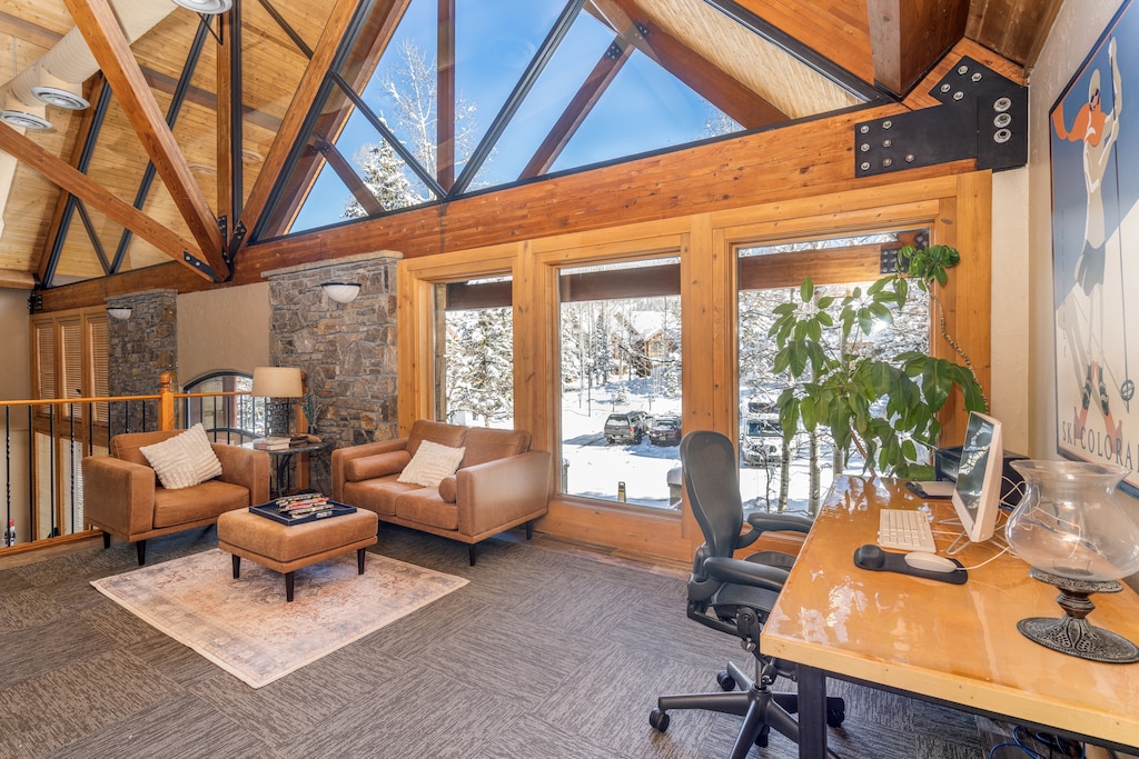 Relax in your stunning living space with vaulted skylights framing snowy mountain views, featuring cozy leather seating and modern workspace.