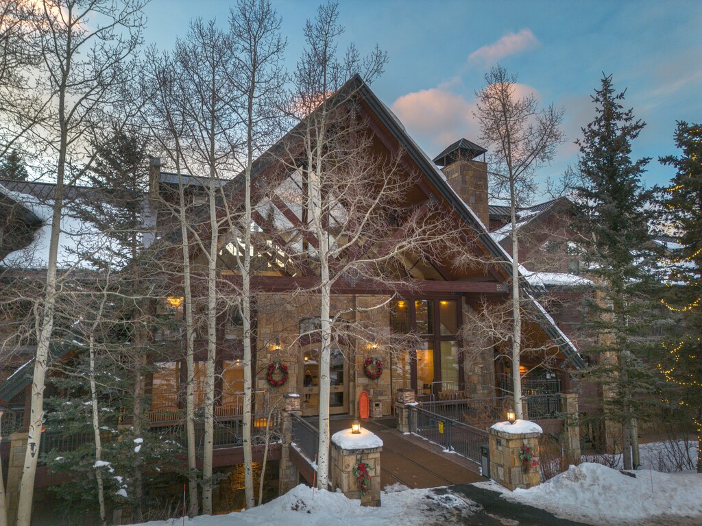 Stunning mountain lodge nestled among snow-dusted aspens, featuring rustic stone architecture and warm holiday touches.