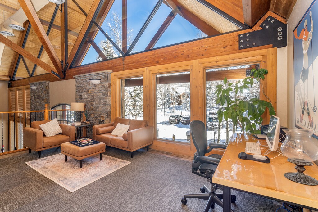 Relax in your stunning living space with vaulted skylights framing snowy mountain views, featuring cozy leather seating and modern workspace.