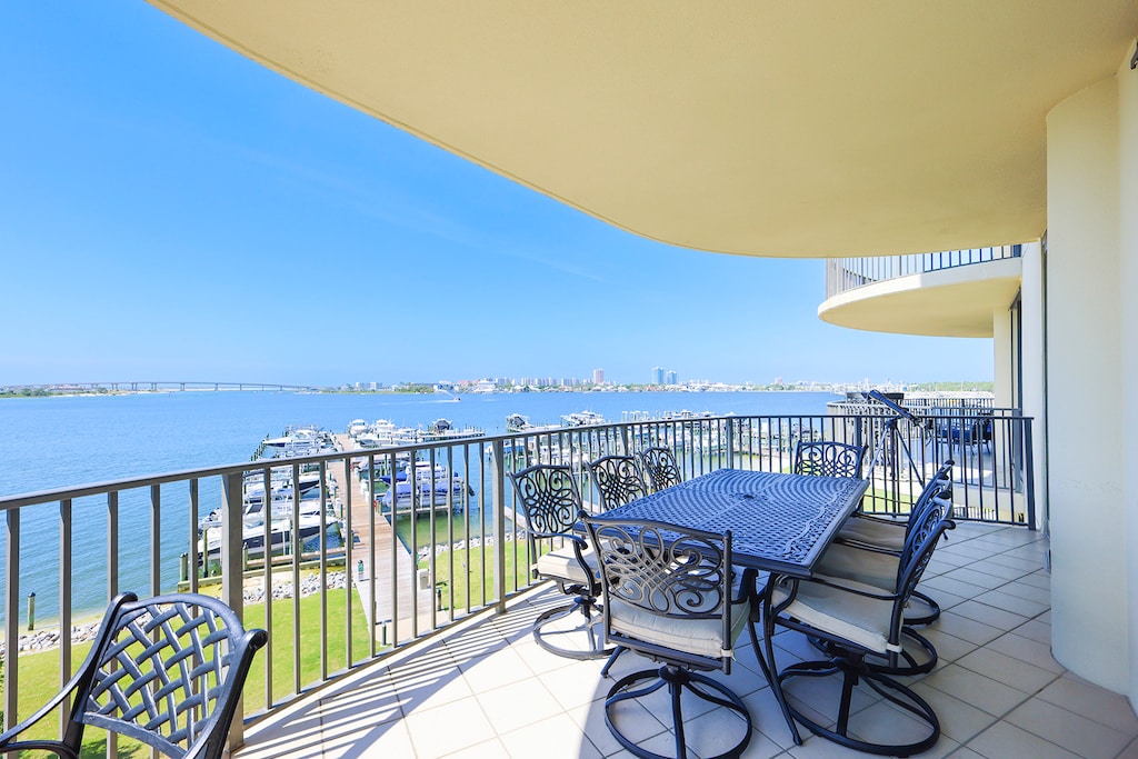 This spacious bay front balcony features a dining table and chairs with a scenic view of the boat marina and serene landscape