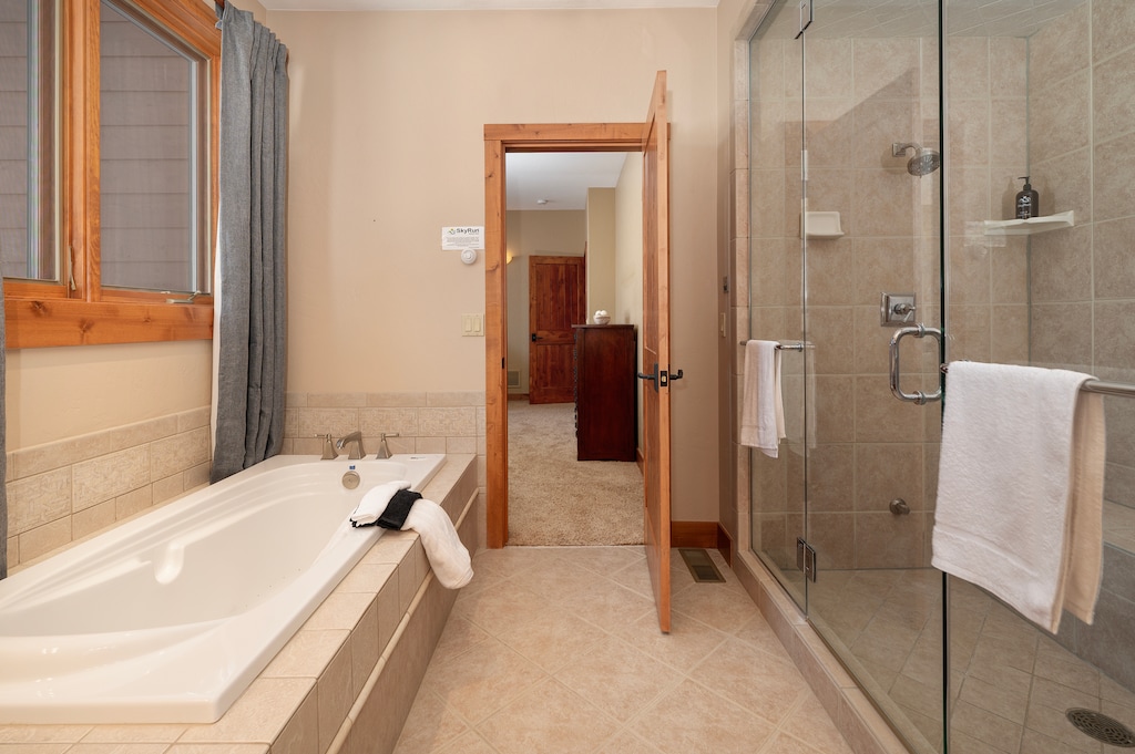 - Unwind in the spa style bath featuring a deep soaking tub and glass shower - Neutral tones, tiled floors, and wood accents enhance the relaxing space - Plush towels and natural light complete the tranquil retreat