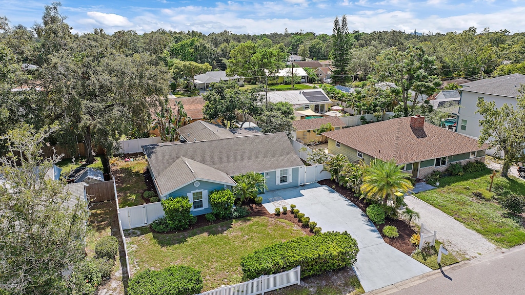 Aerial view of a suburban neighborhood with a blue single-story house, driveway, and landscaped front yard with trees and shrubs.