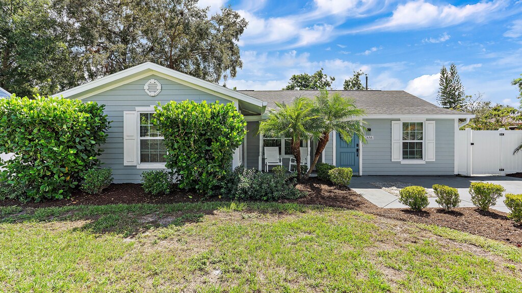 A single-story gray house with white trim, a blue front door, and a well-kept lawn with various shrubs and trees.