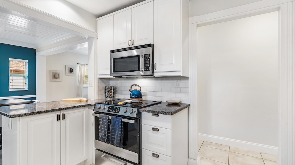 Modern kitchen featuring white cabinets, granite countertops, stainless steel microwave and stove, and a teal kettle on the stove. Blue wall with windows and artwork is visible in the adjoining room.