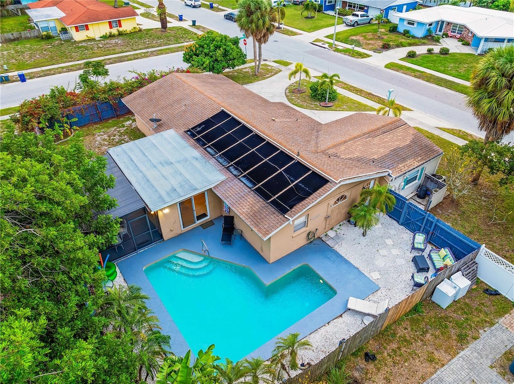 Aerial view of a house with a beige roof featuring a swimming pool in the backyard, partially covered by a screen enclosure, surrounded by other houses and trees on a sunny day.