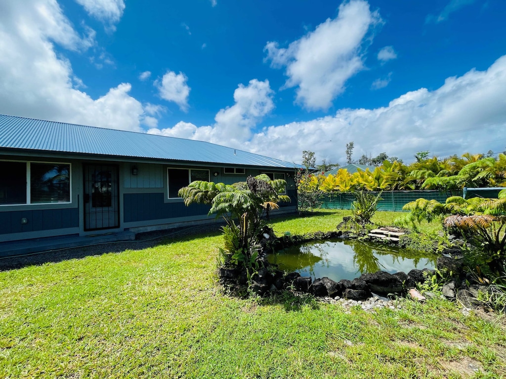 Charming single-story home with a metal roof, surrounded by lush tropical landscaping and featuring a serene private pond in the front yard.