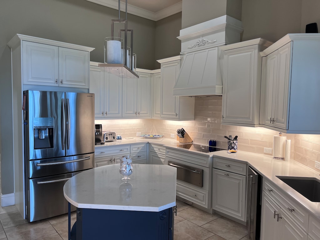 Modern kitchen with white cabinetry, stainless steel appliances, a central island, and a tiled backsplash. The space is well-lit with under-cabinet lighting and a contemporary pendant light.