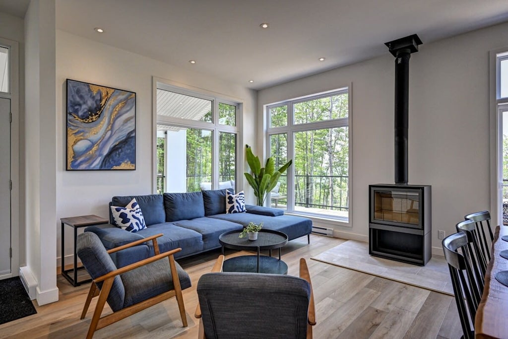 Bright living area with large windows, a wood-burning indoor fireplace, and forest views