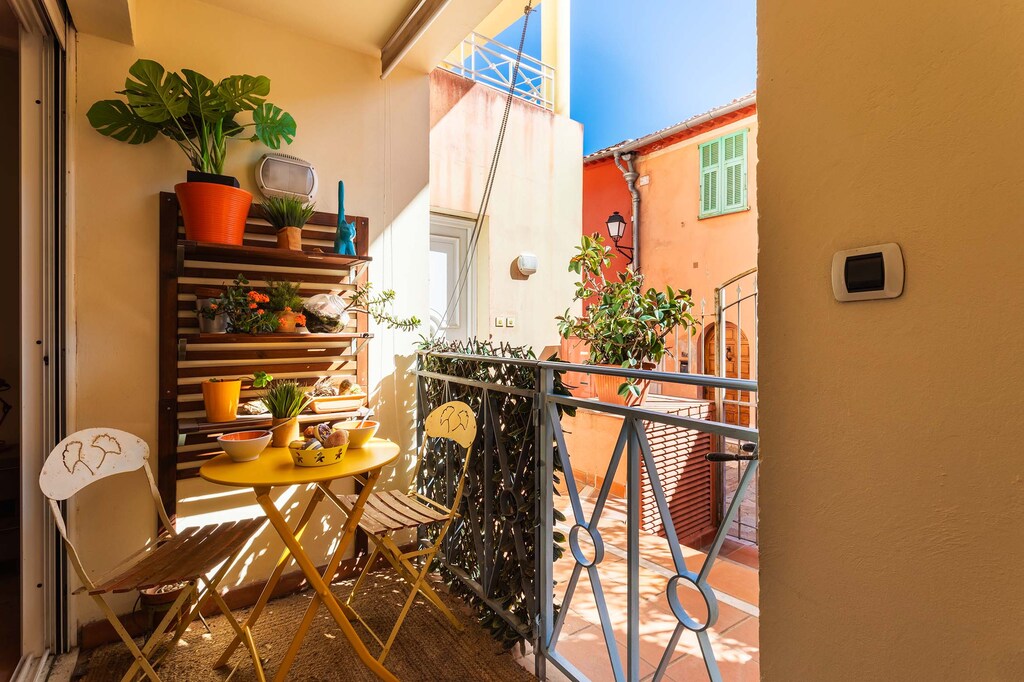 Charming sunny balcony with colorful table and chairs, lush plants, and peaceful views. Perfect for outdoor relaxation.