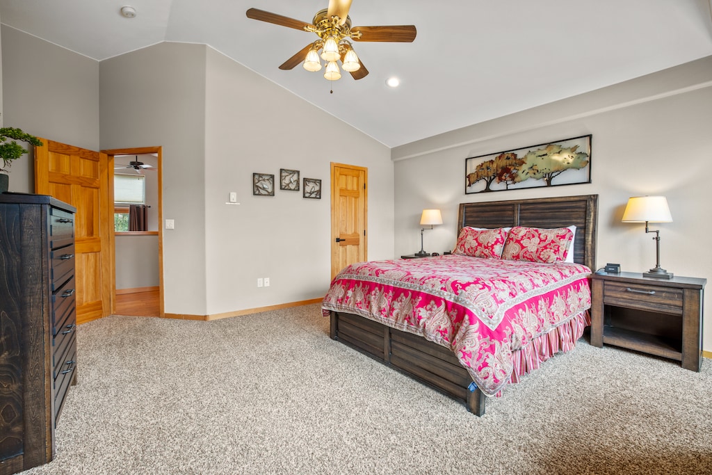 Elegant primary bedroom featuring a vaulted ceiling with ceiling fan, plush carpeting, and stylish decor. A bright and inviting retreat with mountain charm.