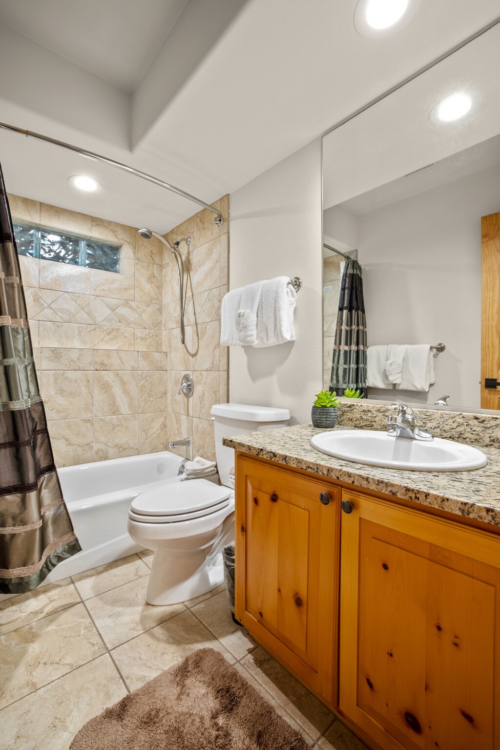 Stylish guest bathroom featuring a granite countertop vanity, tiled shower-tub combination, and warm wood cabinetry for a cozy mountain feel.