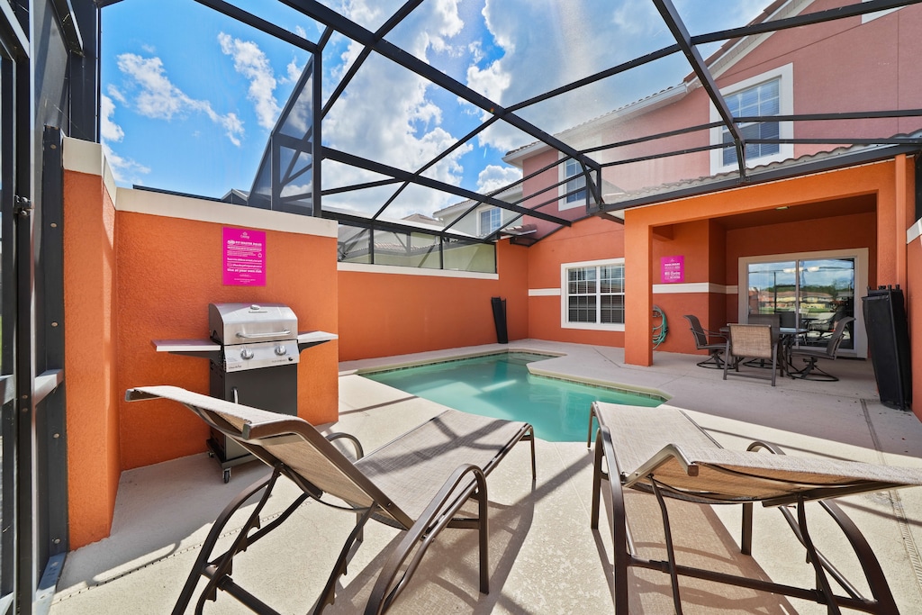 - Outdoor patio with a private pool, perfect for relaxing under a screened enclosure - Comfortable lounge chairs and a gas grill offer options for both sunbathing and outdoor cooking - Bright orange walls and sunny weather create a vibrant atmosphere