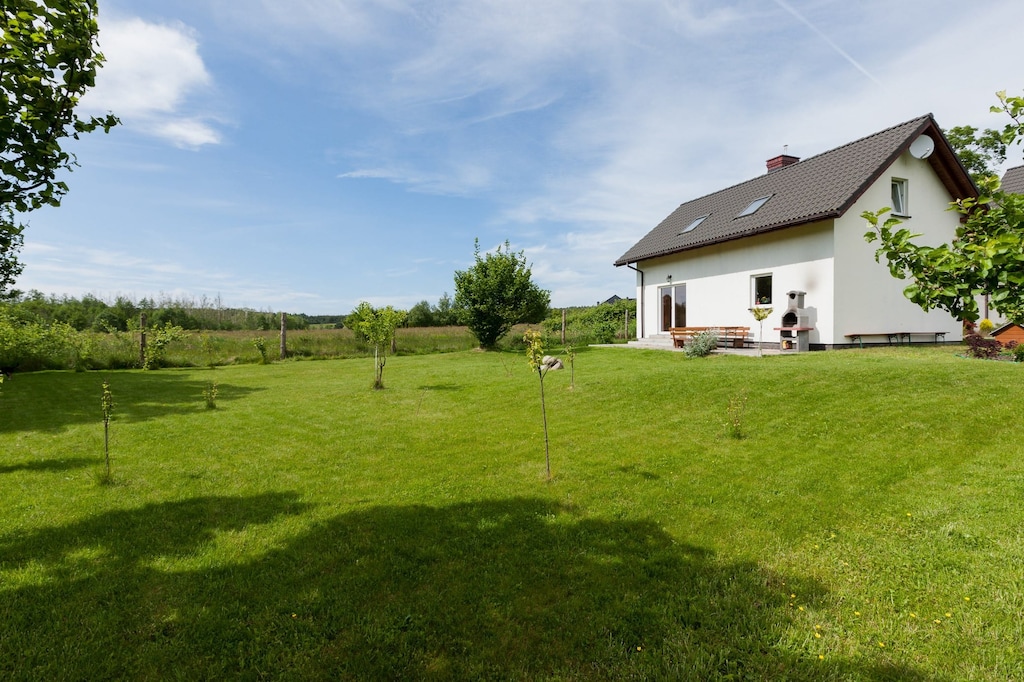 A spacious garden with a lush green lawn surrounds the white house, creating a peaceful spot for outdoor relaxation.