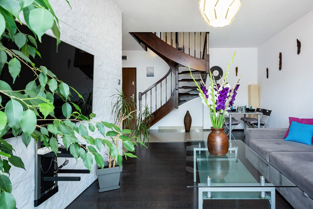Another angle of the living room, showcasing a contemporary design with a mix of greenery, stylish vases, and an open staircase leading to an upper level.