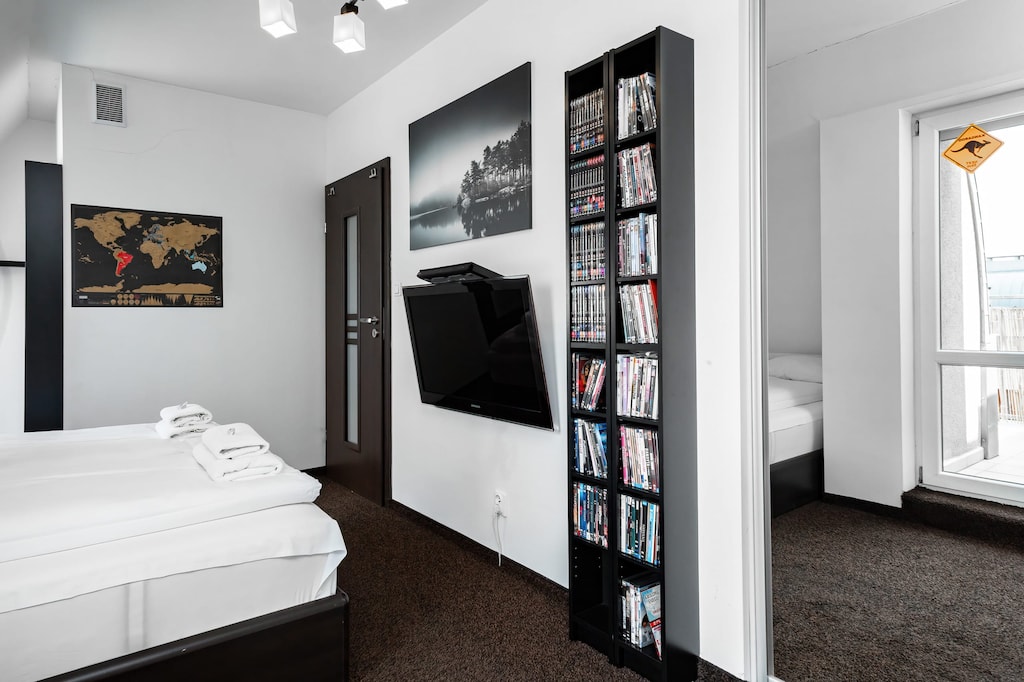 A bright bedroom with a double bed adorned with crisp white linens, slanted ceilings, and a large window allowing sunlight to flood the space.