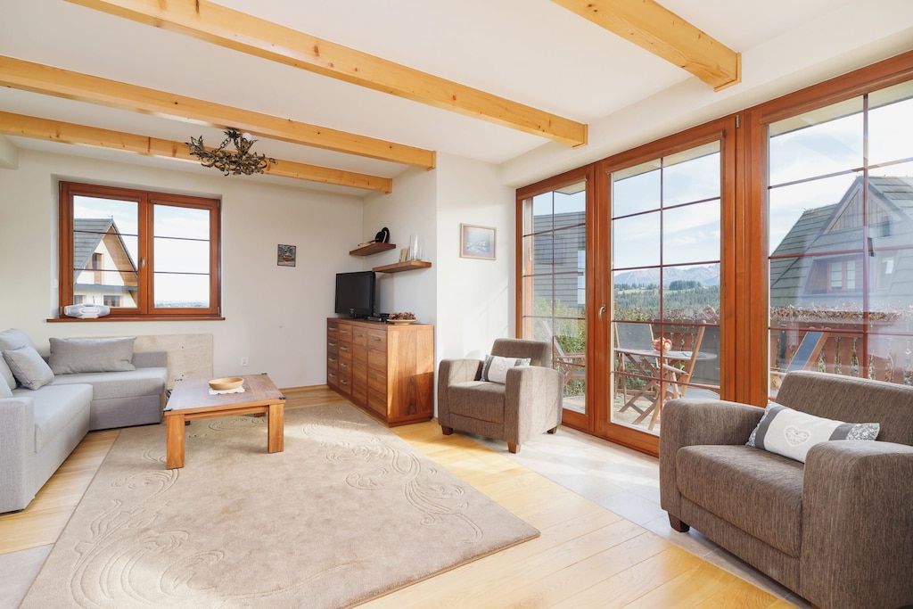 Another angle of a living area with a sofa set, coffee table, and wooden beams on the ceiling. A door leads to an outdoor balcony.