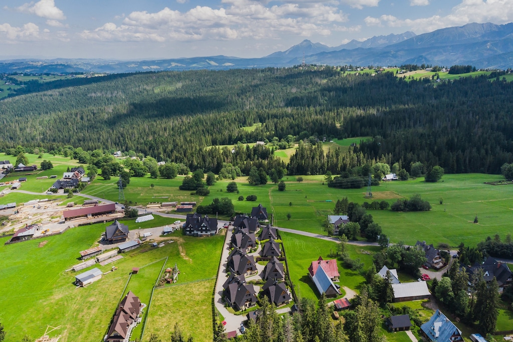 A scenic aerial view of a village with green fields, houses, and surrounding hills.